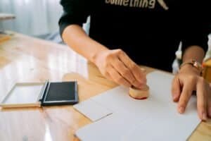Close-up of hands stamping a document on a wooden desk indoors.